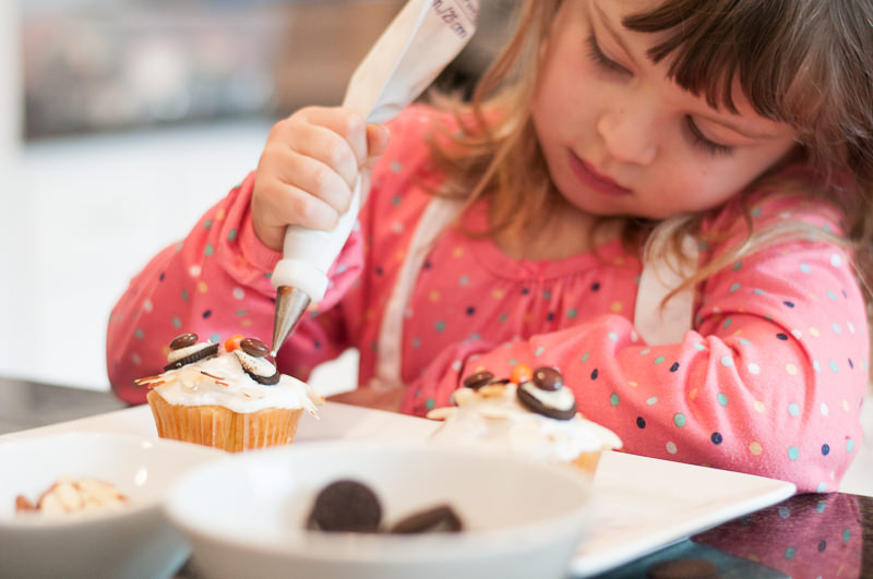 young girl decorating cupcakes with frosting bag, Plymouth MI Child Photographer